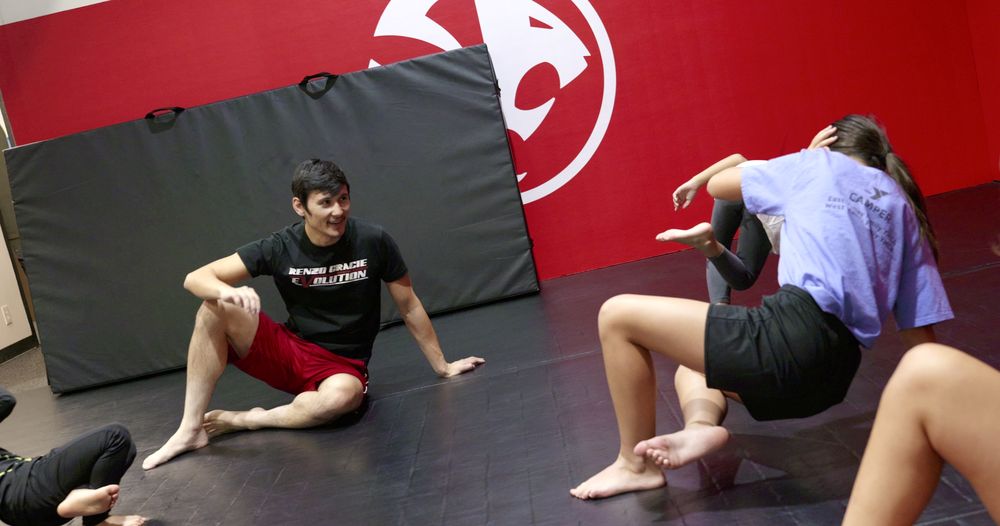 Instructor seated on the mat coaching a young Kids Jiu Jitsu student one-on-one at Renzo Gracie Evolution
