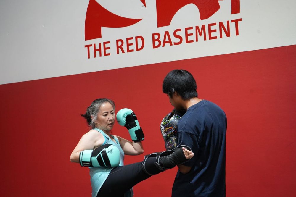 Adult Muay Thai student in teal gloves punching focus mitts held by a partner at Renzo Gracie Evolution