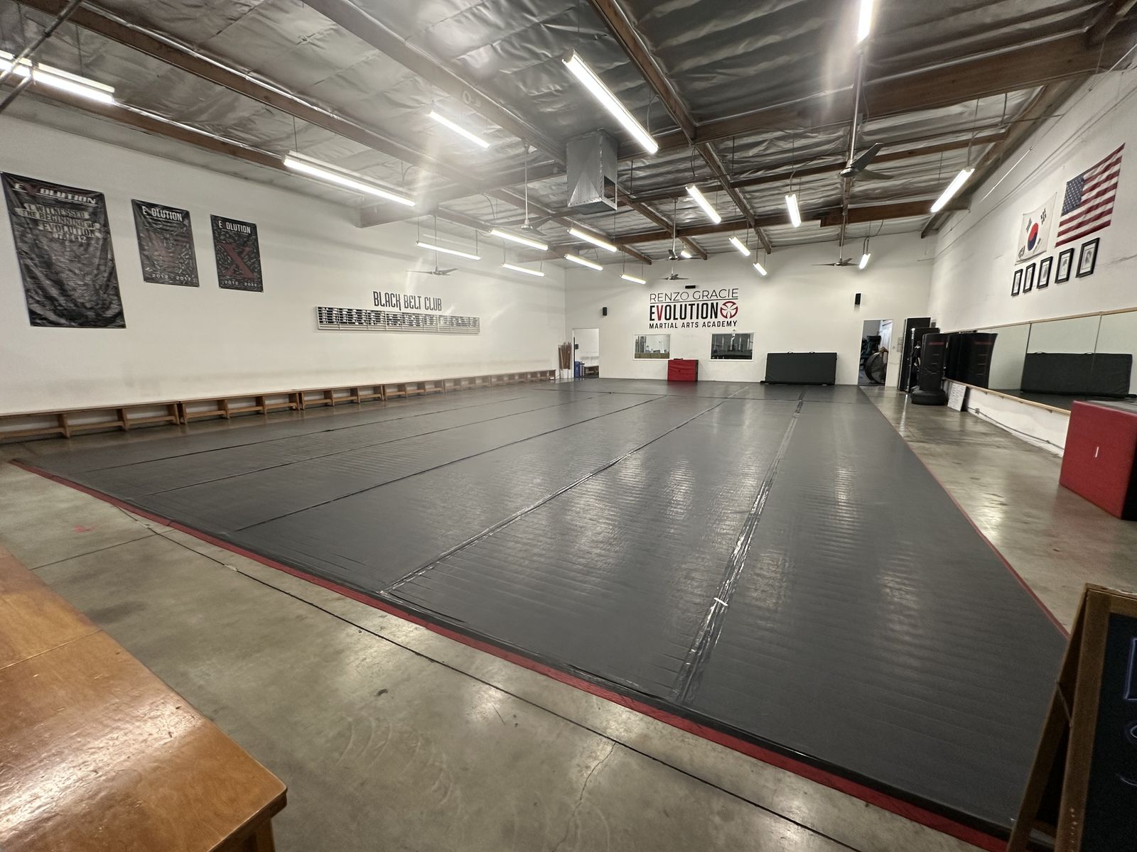 Main training mat at Renzo Gracie Evolution in Chatsworth seen from the corner, with the academy wall sign and flags